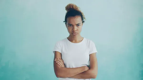 A frustrated woman with folded arms against a blue background
