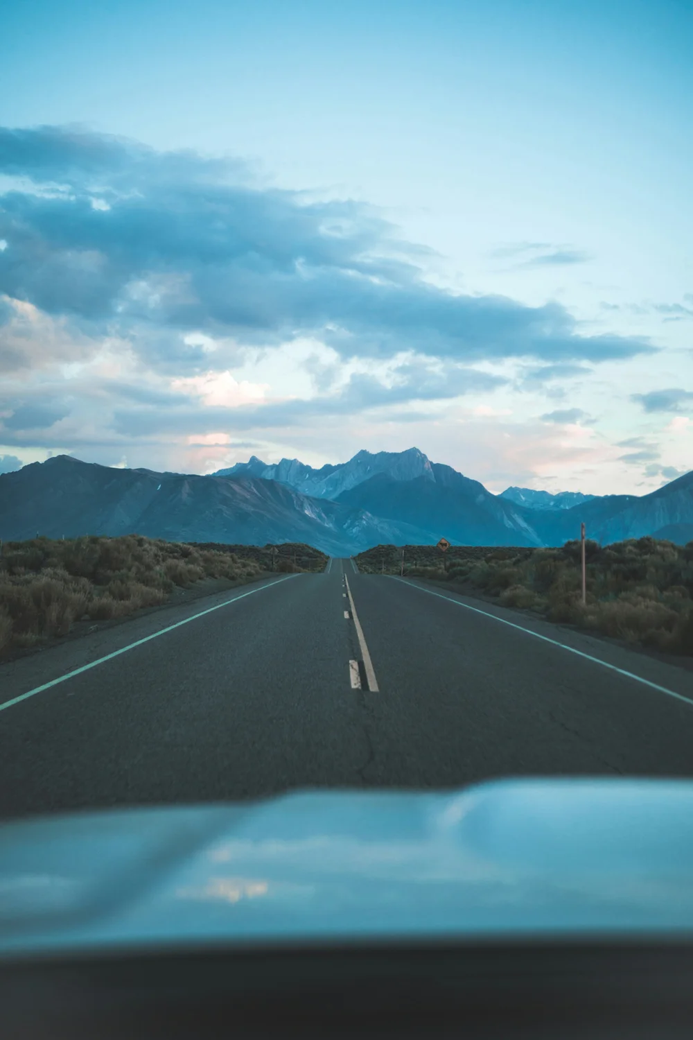 A road stretching forward into open sky with mountains in the background